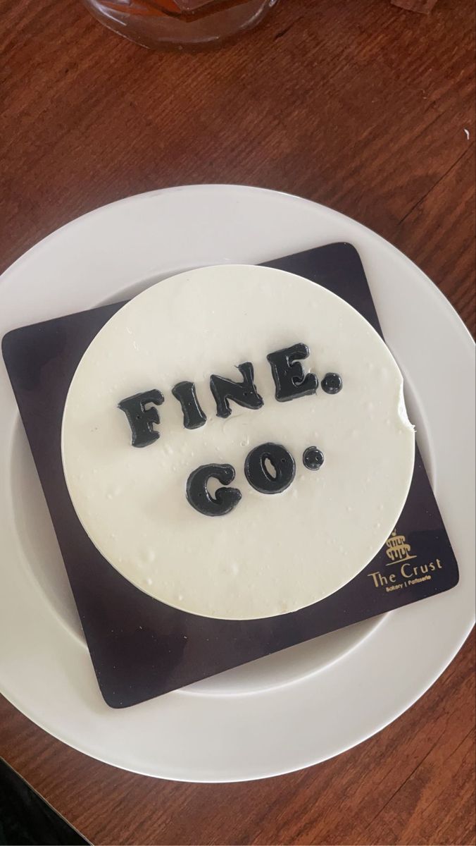 a cake with the words fine go written on it sitting on a plate next to a glass of wine