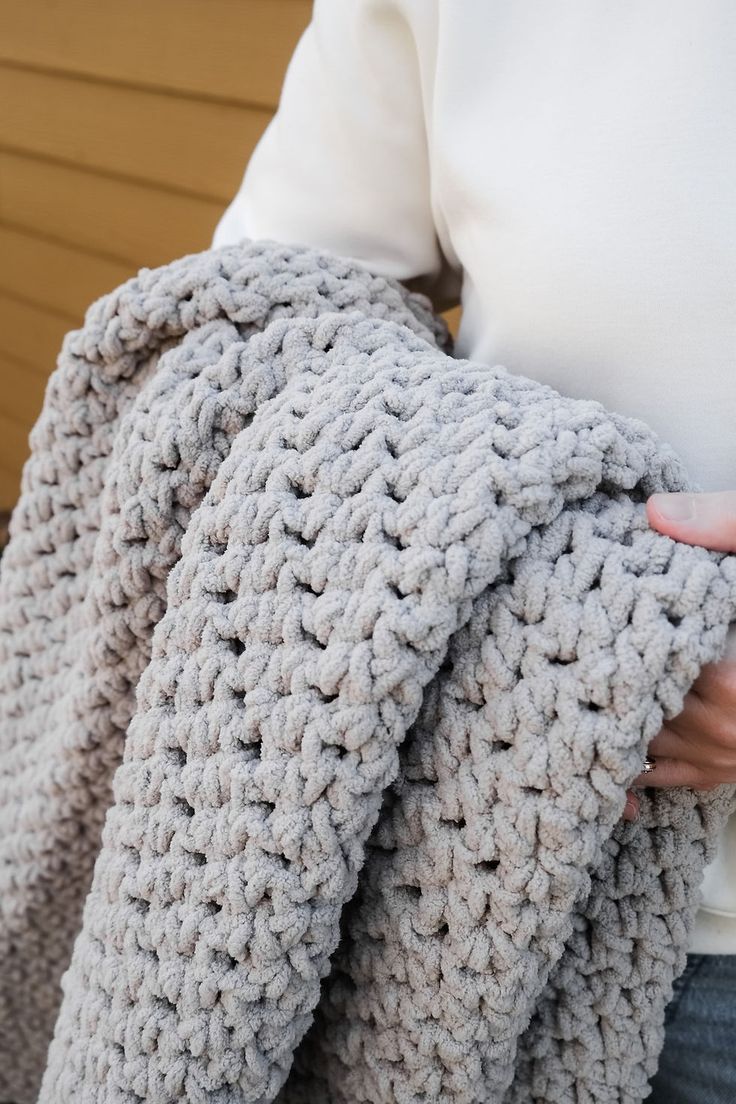 a woman is holding a crocheted blanket in her hands