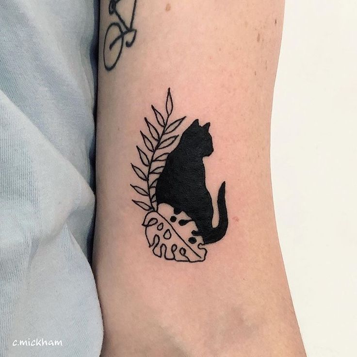 a black cat tattoo on the left ankle and right leg, with leaves around it