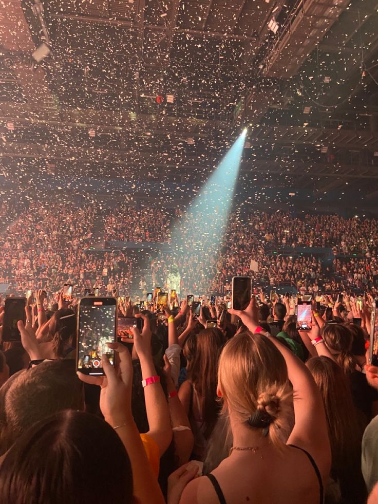 a large crowd at a concert with confetti falling from the ceiling and people holding up their cell phones