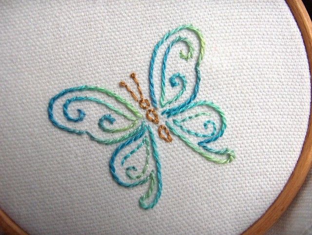 a close up of a cross stitched butterfly on a white fabric with blue and green accents