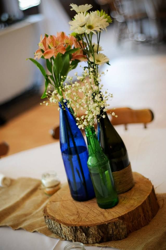 three blue vases with flowers are sitting on a wooden slice in front of a white table cloth