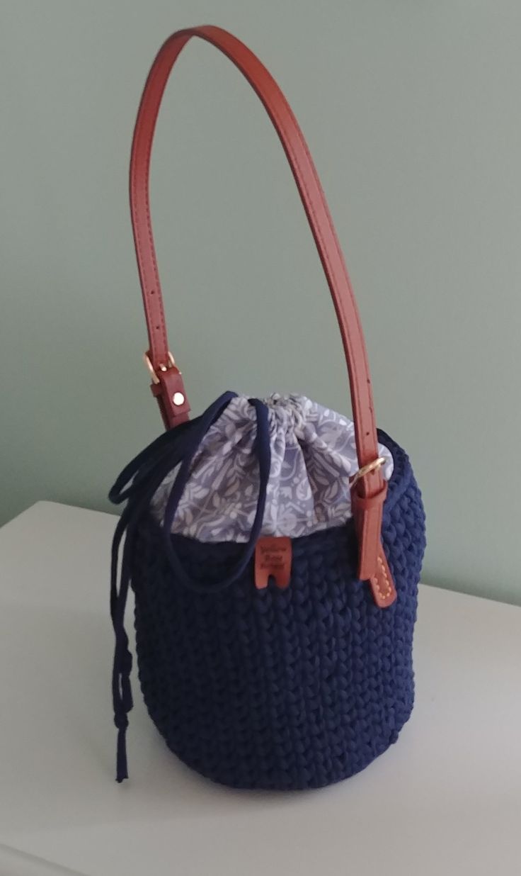 Navy Bucket Bag. Crocheted navy blue bucket bag, cotton blue and white fabric lining, inside pockets, drawstring closure, and brown leather buckle strap.  Dimensions: 23 inches round, 7.25 inches deep, 12 inch strap drop.  Surface washable.  Thank you for visiting YellowRoseRetail.com! Casual Blue Crossbody Bucket Bag, Blue Tote Bucket Bag, Blue Tote Bucket Bag With Handles, Blue Satchel Bucket Bag With Dust Bag, Casual Blue Bucket Bag With Removable Pouch, Blue Bucket Bag For Shopping, Blue Canvas Bucket Bag For Daily Use, Casual Blue Bucket Bag With Adjustable Strap, Blue Canvas Bucket Bag