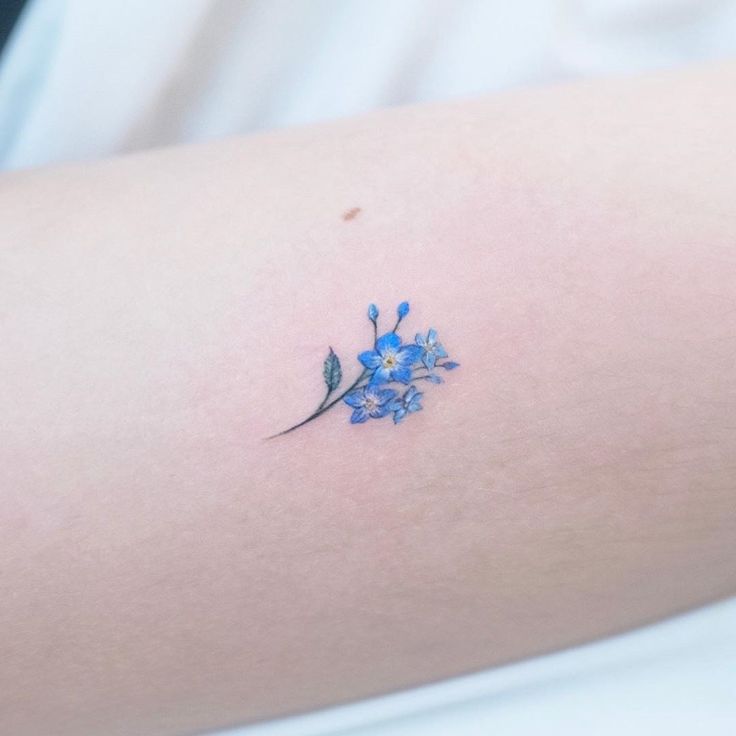 a small blue flower on the back of a woman's arm