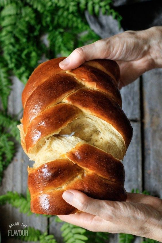 a person holding a loaf of bread in their hand on top of a wooden table