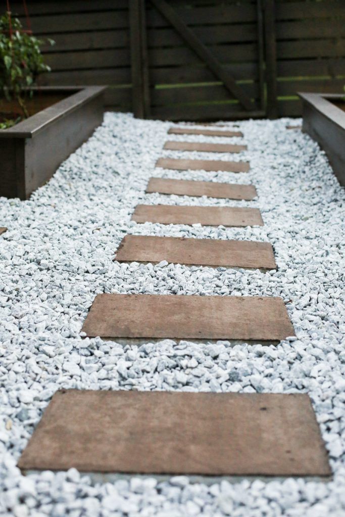 a pathway made out of stones in front of a wooden fence and planter box