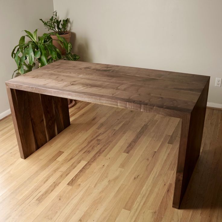 a wooden table sitting on top of a hard wood floor next to a potted plant