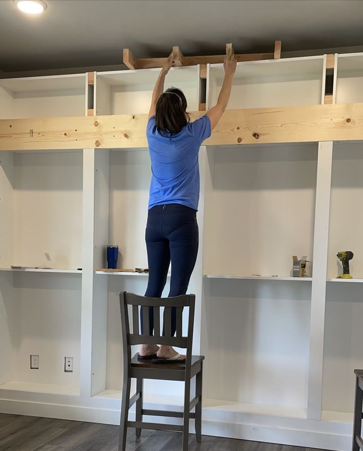 a woman standing on top of a chair in front of a shelf with bookshelves