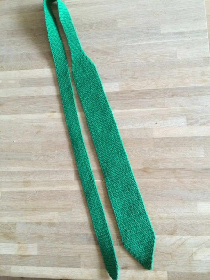 a green knitted tie laying on top of a wooden floor next to a knife