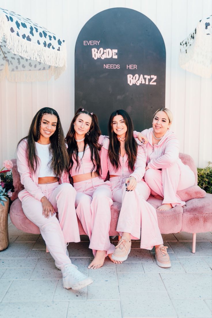 four women sitting on a pink couch in front of a sign