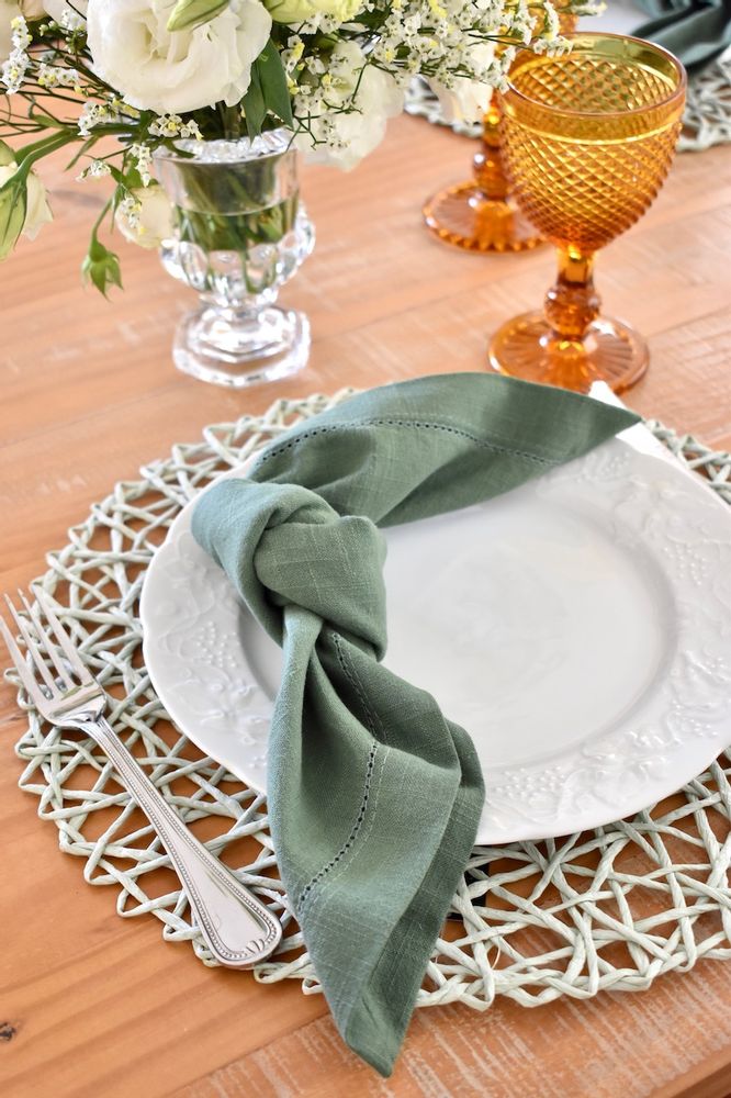 a white plate with a green napkin sitting on top of it next to a glass vase filled with flowers