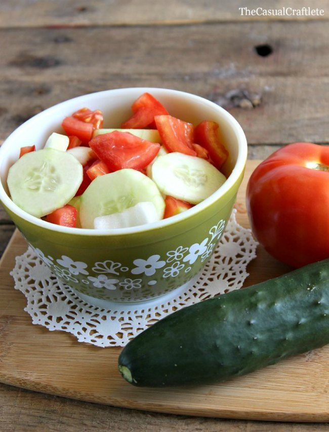 cucumbers, tomatoes and other vegetables in a bowl on a cutting board