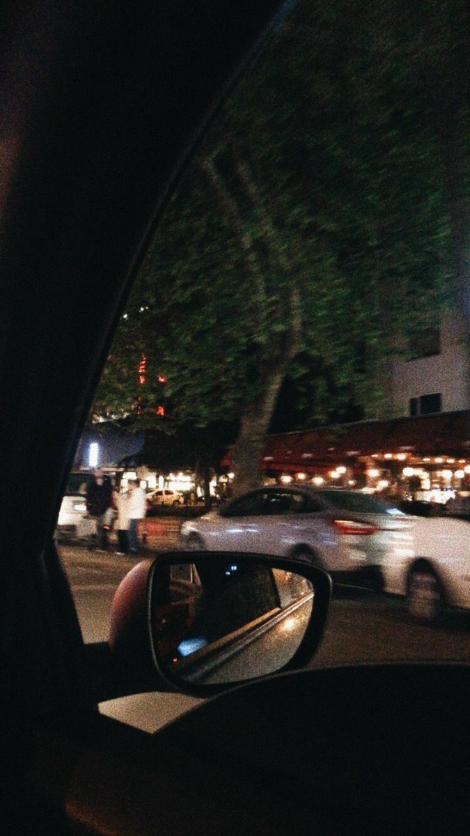 a car is driving down the street at night with its rear view mirror showing it's reflection