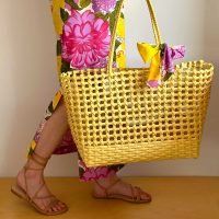 a woman carrying a yellow basket with pink flowers on the bottom and side, while standing in front of a white wall