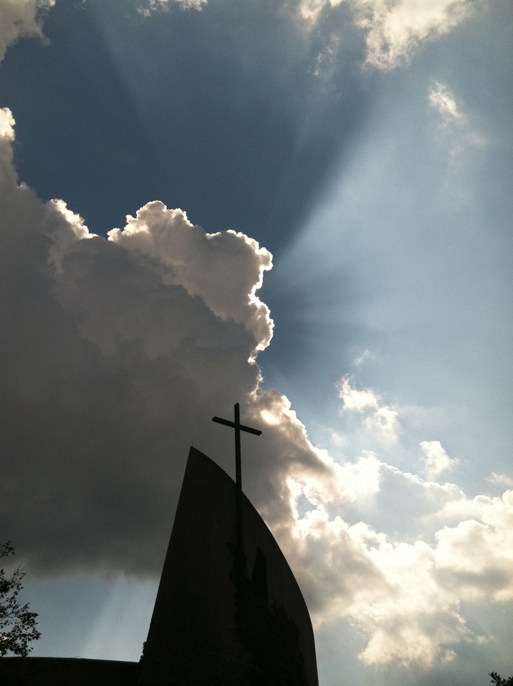 the sun shines through clouds behind a church steeple with a cross on it