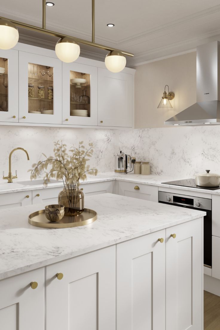 a white kitchen with marble counter tops and gold accents on the cabinets, along with brass pulls