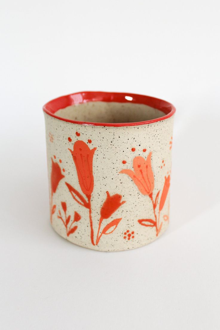 a red and white cup with flowers painted on the inside is sitting on a white surface