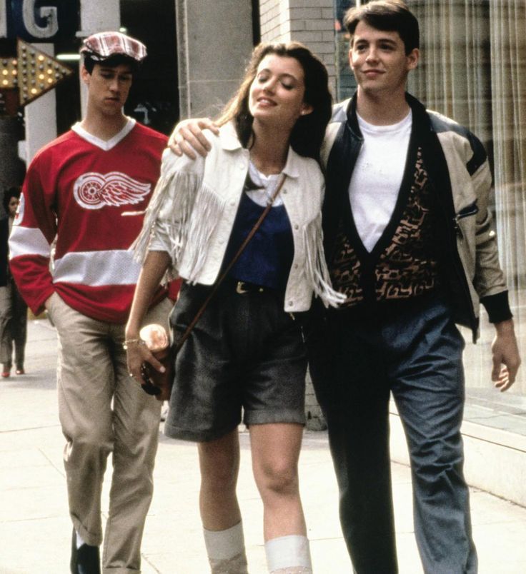 two men and a woman walking down the street with one man holding his arm around the other