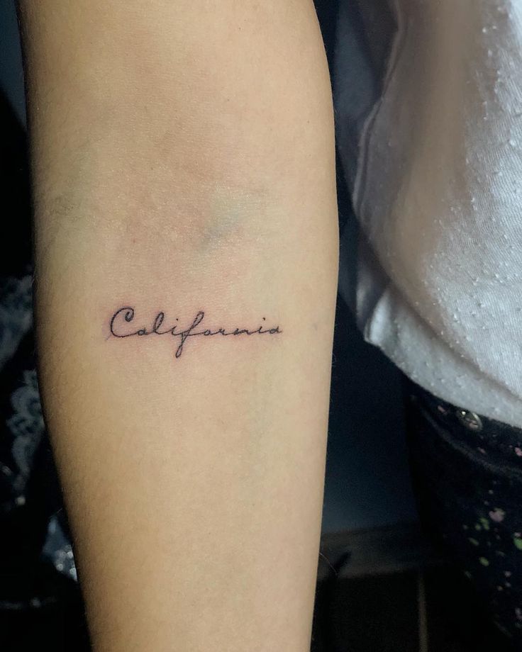 a woman's arm with the word california tattooed on her left forearm and in cursive font