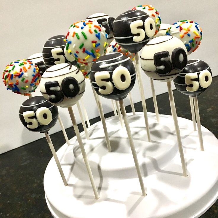 cake pops decorated with numbers and sprinkles on a white stand in front of a wall