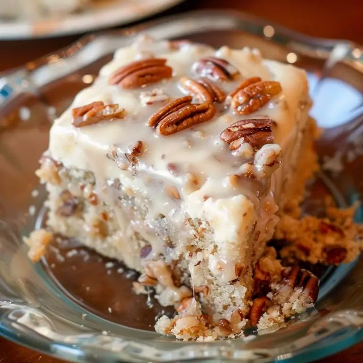 a piece of cake on a glass plate with pecans around the edges and frosting