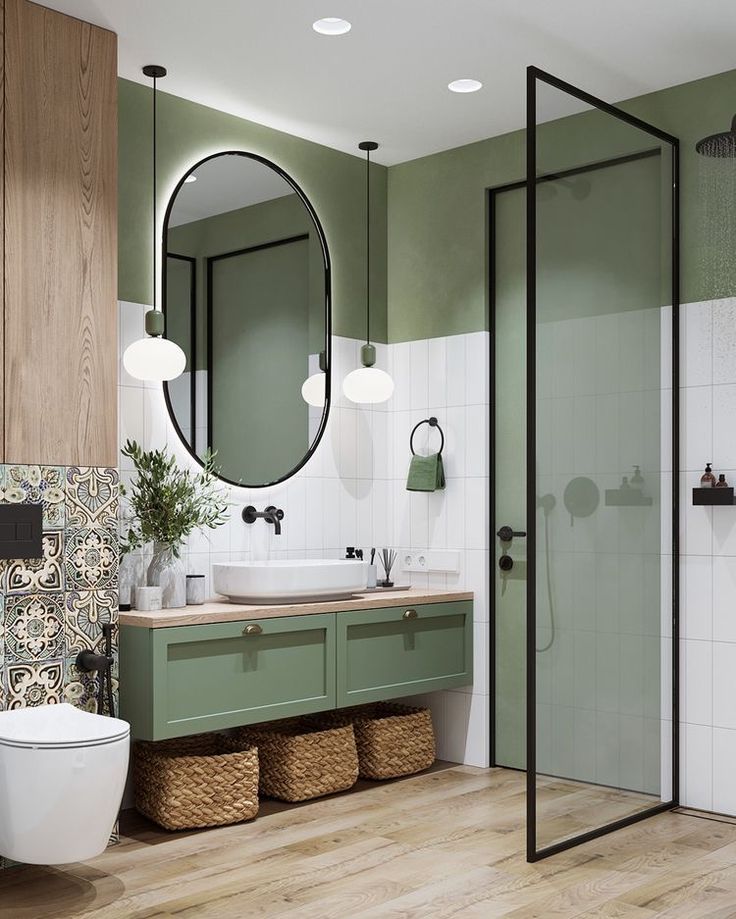 a bathroom with green and white walls, wooden floors and a round mirror above the sink