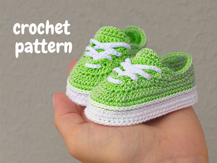 a hand holding a crochet green and white baby sneaker with the words crochet pattern on it