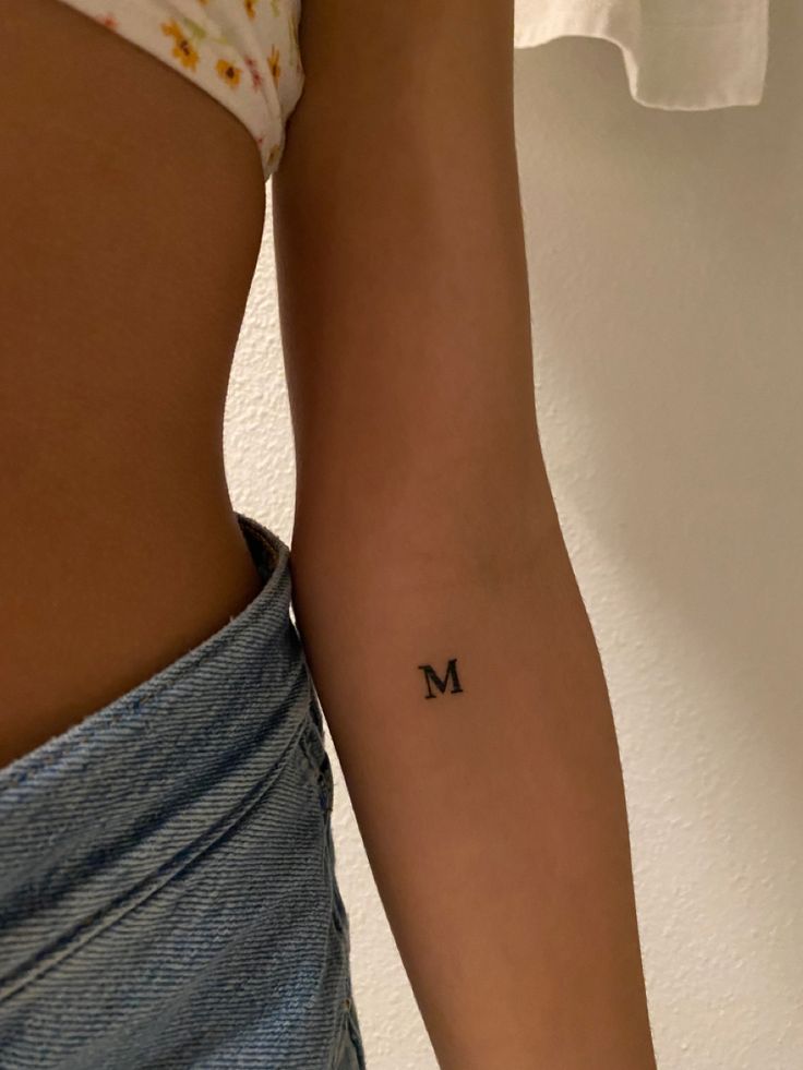 a woman's lower arm with the letter m tattooed on her left side, in black ink