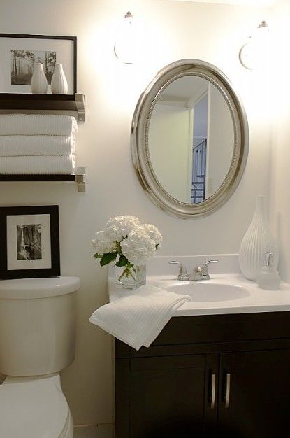 a white toilet sitting next to a sink in a bathroom under a round mirror and framed pictures on the wall