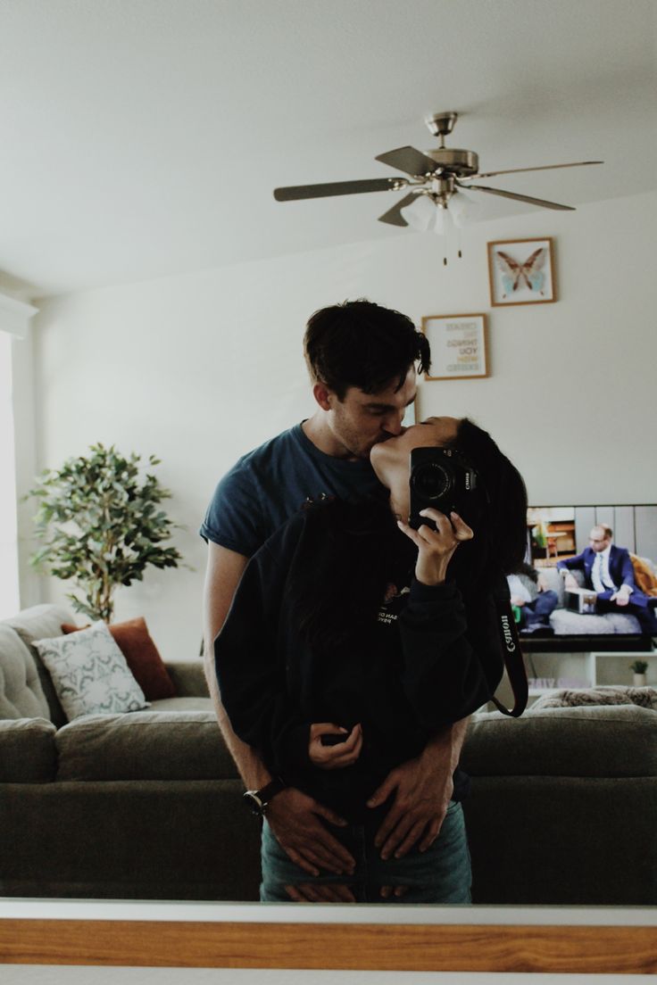 a man and woman standing in front of a couch taking a photo with a camera