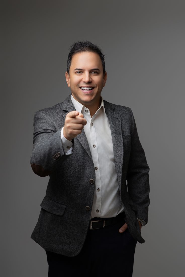 a man in a suit is pointing his finger at the camera while standing against a gray background