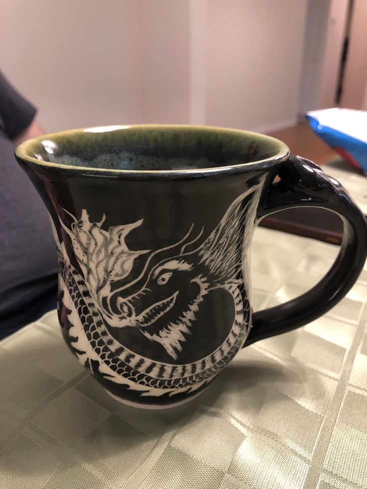 a black and white coffee cup sitting on top of a table next to a blue pillow