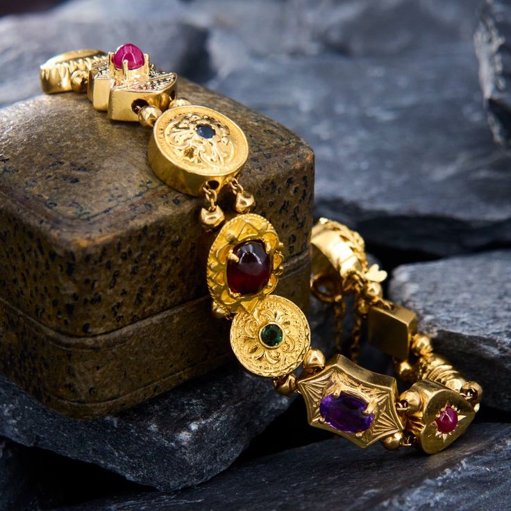 This circa 1950s slide bracelet features thirteen (13) charms that alternate with pairs of 3.1mm polished gold beads. The charms are prong/bezel set with a 1 seed pearl, 4 round cut sapphires, 2 round cabochon cut rubies, 1 oval cut amethyst, 1 round cut green tourmaline, 1 oval cabochon cut garnet, 1 round brilliant cut diamond, 2 round cut emeralds, and 3 round white opal cabochons. The bracelet measures 12.5mm wide and will fit up to a 7 inch wrist.  It is finished with a round filigree slide clasp that is bezel set with one (1) round brilliant cut diamond.  There is a safety chain for extra security. Slide Bracelet, Safety Chain, Seed Pearl, Green Tourmaline, White Opal, Oval Cabochon, Round Brilliant Cut Diamond, Gold Beads, Oval Cut