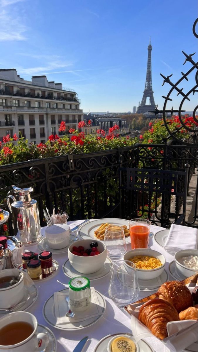 a table topped with plates of food next to a balcony overlooking the eiffel tower