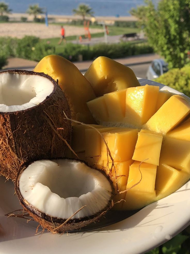 a white plate topped with cut up coconuts and sliced mangoes on top of it