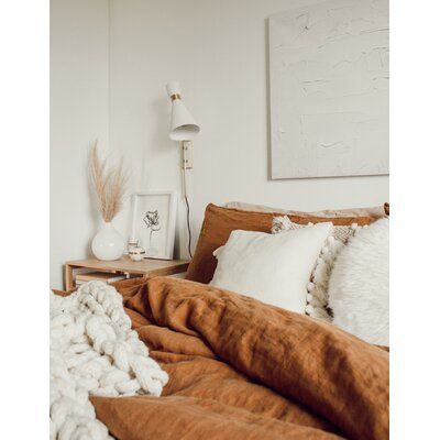 a bed with blankets and pillows on top of it next to a nightstand in a white room