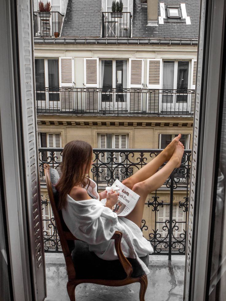 a woman sitting in a chair on top of a balcony next to a tall building