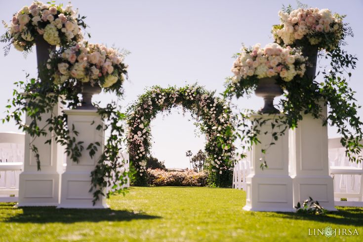 an outdoor ceremony setup with white chairs and flowers on the pillars, in front of a blue sky