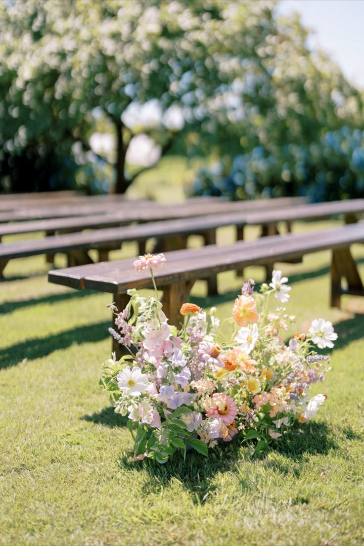 an arrangement of flowers sits in the grass next to wooden benches