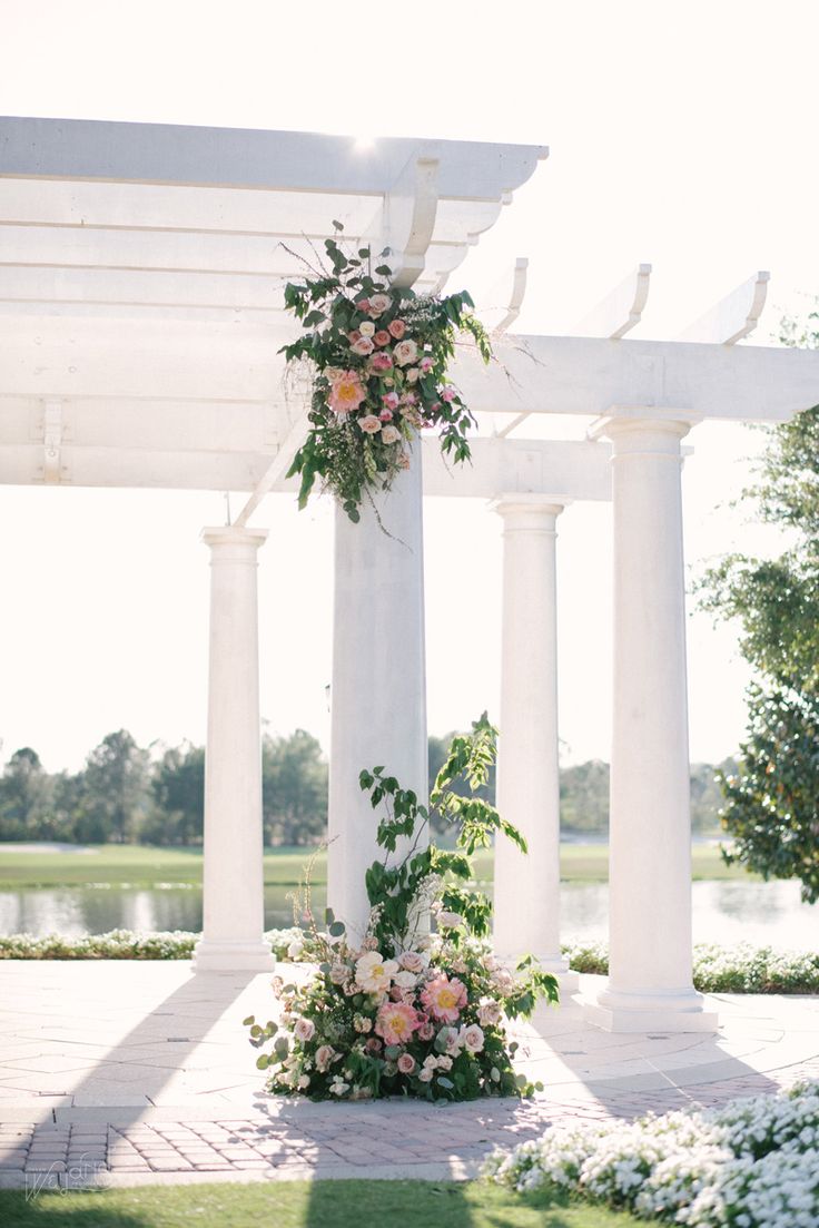 an outdoor wedding setup with flowers and greenery on the columns, in front of a lake