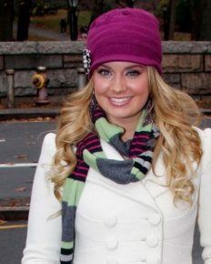 a beautiful young blond woman wearing a white coat and purple hat with a scarf around her neck