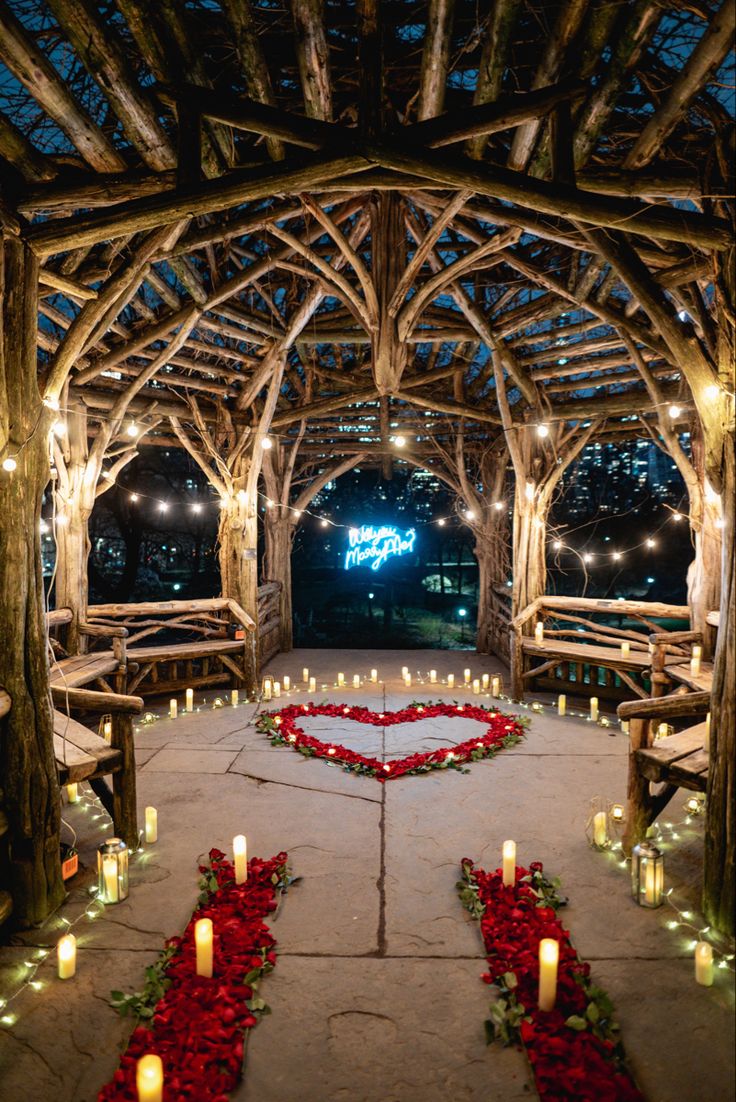 an outdoor wedding venue with candles and roses on the floor, surrounded by wooden arches