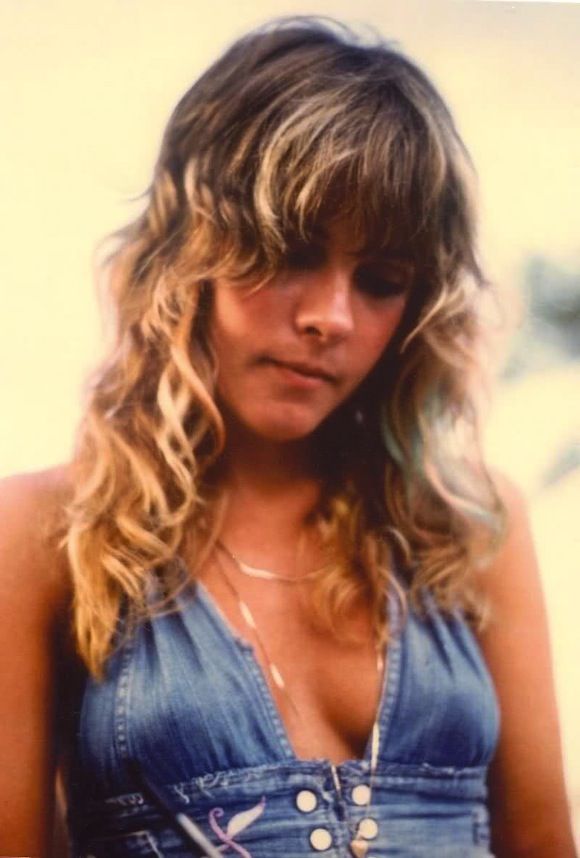 a black and white photo of a woman with long hair wearing overalls, looking at the camera