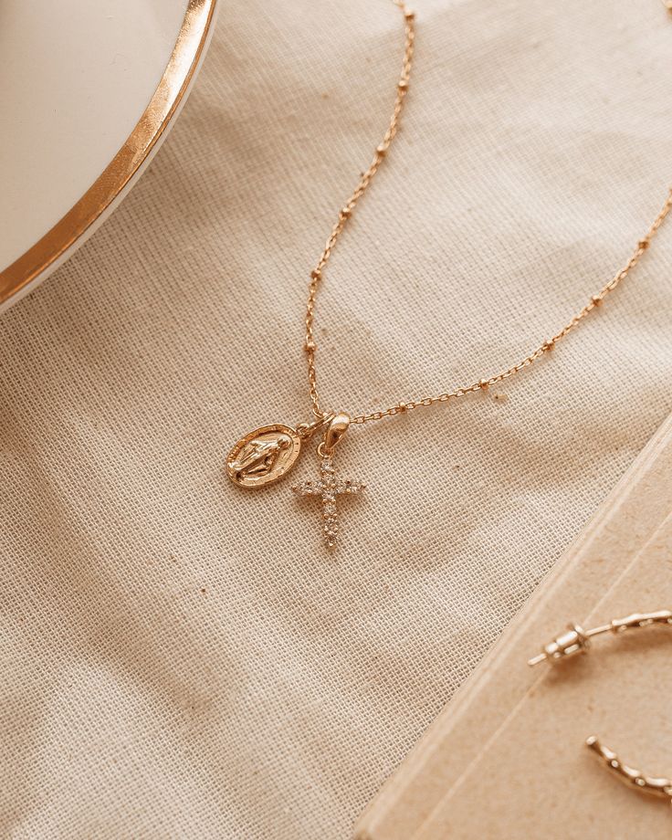 The Protégée Necklace means protected in French. This delicate charm necklace with Madonna and her cross are both iconic and beautiful, reminding you that you are protected. The Madonna pendent is gold plated silver 8x13.5mm and 2mm thick. Petite rhinestone cross features Cubic Zirconia on gold plated silver 10.5x15.5x2mm. Gold Filled chain 18 inches. Madonna Jewelry, Cross Necklace Women, Parisian Wedding, Cross Jewelry Necklace, The Madonna, Christian Necklace, Catholic Jewelry, Rhinestone Cross, Gold Cross Necklace