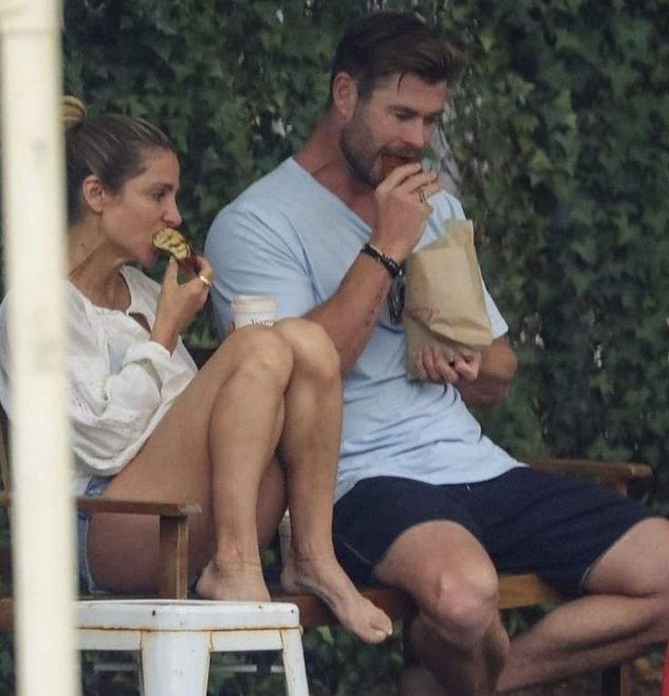 a man and woman sitting on a bench eating food