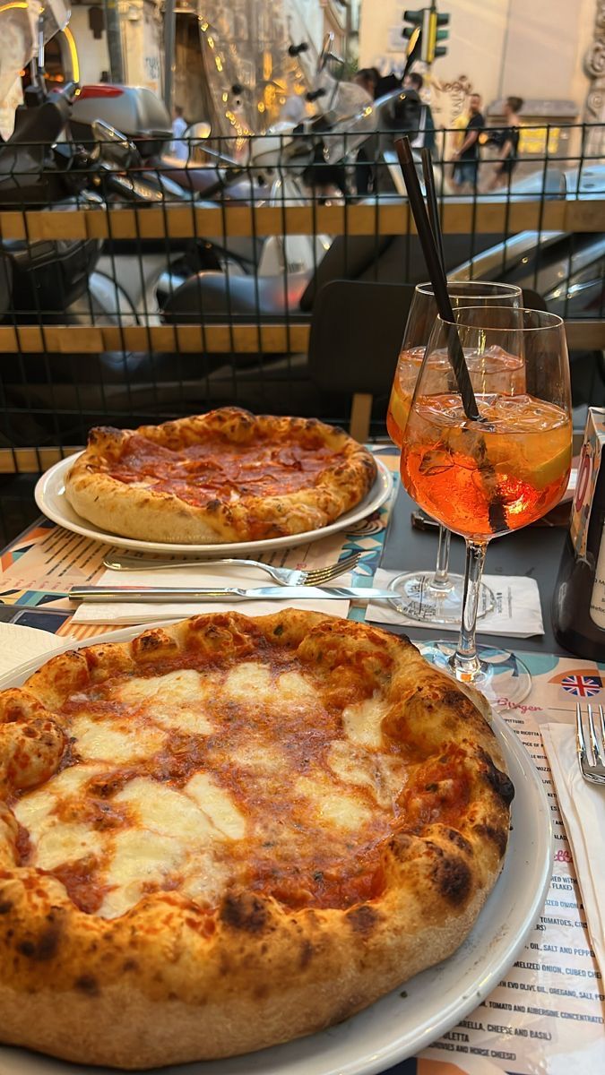 two pizzas sitting on top of white plates next to glasses and utensils