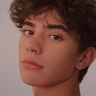 a close up of a young man with curly hair looking at the camera and to his left