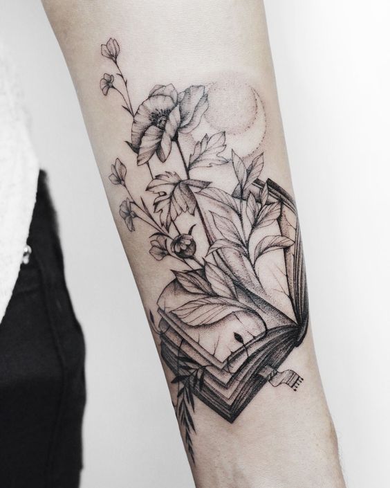 a woman's arm with a book and flowers tattoo on the left side of her arm