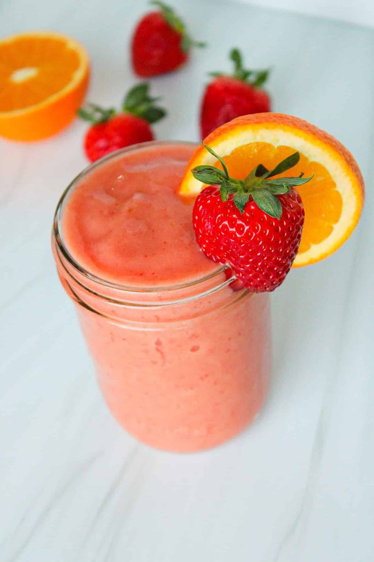 a strawberry orange smoothie is garnished with an orange slice and fresh strawberries