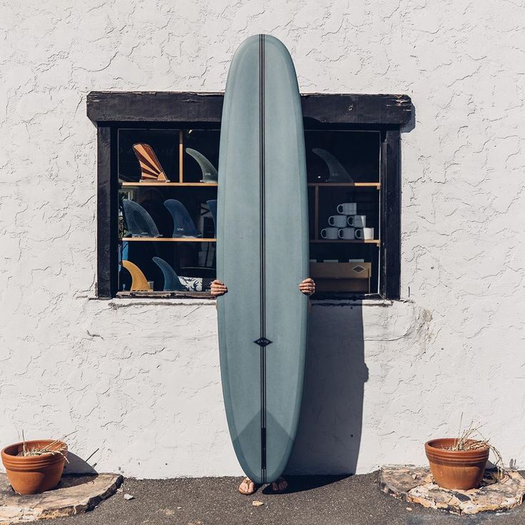 a surfboard leaning up against a white wall with potted plants in the window